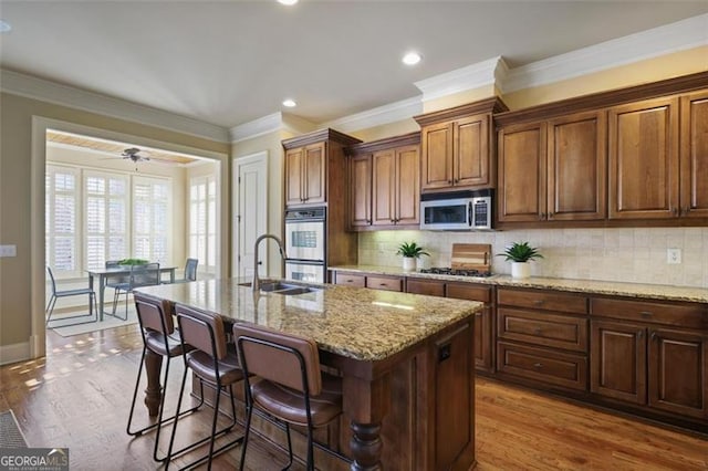 kitchen with appliances with stainless steel finishes, tasteful backsplash, sink, ceiling fan, and a center island with sink