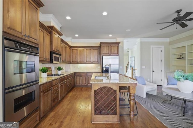 kitchen featuring sink, stainless steel appliances, a kitchen breakfast bar, light stone counters, and a center island with sink