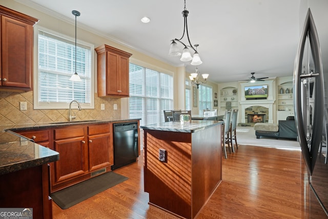 kitchen with dark wood-type flooring, sink, dishwasher, a stone fireplace, and hanging light fixtures