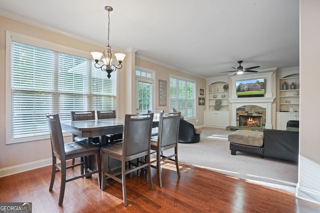 dining room featuring built in features, dark hardwood / wood-style floors, crown molding, a fireplace, and ceiling fan with notable chandelier