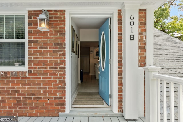 entrance to property featuring brick siding and roof with shingles