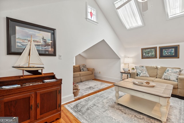 living area featuring a skylight, wood finished floors, baseboards, and high vaulted ceiling