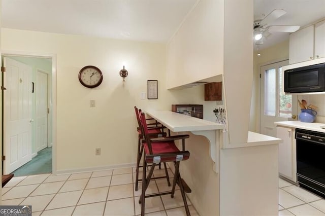 kitchen with white cabinetry, a kitchen breakfast bar, kitchen peninsula, light tile patterned floors, and black appliances