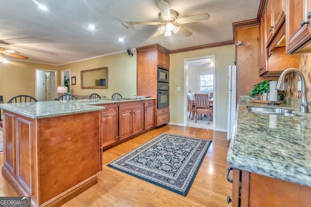 kitchen with black appliances, sink, light hardwood / wood-style floors, light stone counters, and kitchen peninsula