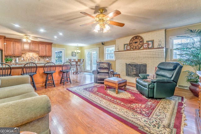 living room featuring a brick fireplace, ceiling fan, a textured ceiling, and light wood-type flooring