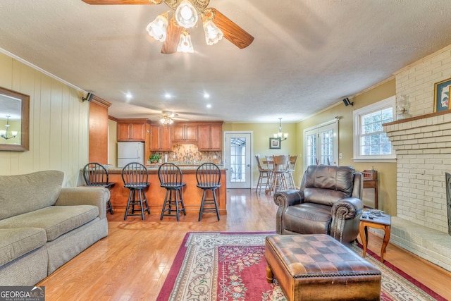 living room featuring crown molding, light hardwood / wood-style flooring, a textured ceiling, and a brick fireplace