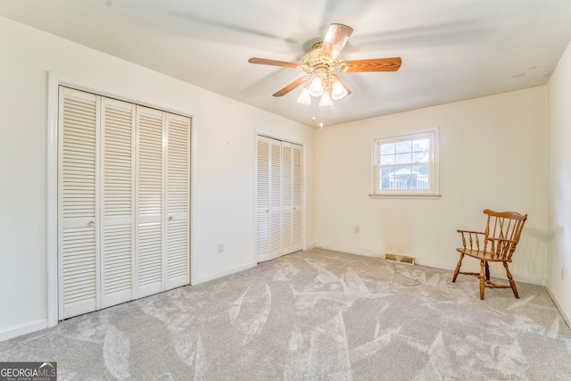 unfurnished bedroom with multiple closets, ceiling fan, and light carpet