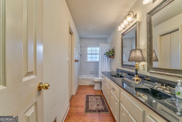 full bathroom with hardwood / wood-style floors, shower / bath combo, vanity, toilet, and a textured ceiling