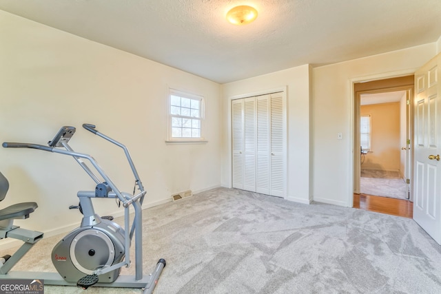 exercise area featuring a textured ceiling and light colored carpet