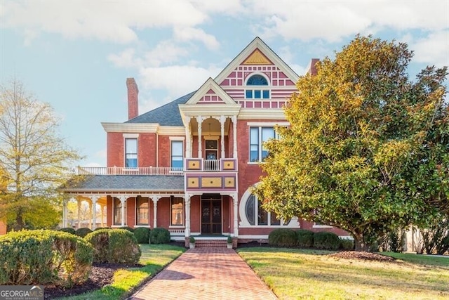 victorian house featuring a balcony and a front lawn