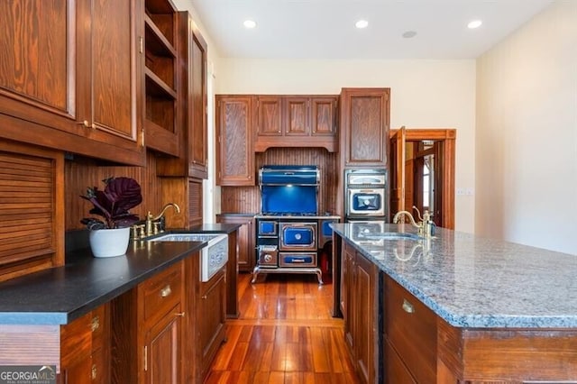 kitchen with a kitchen island with sink, sink, oven, and dark wood-type flooring