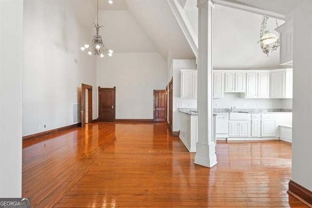 interior space featuring a notable chandelier, light hardwood / wood-style floors, ornate columns, and a high ceiling