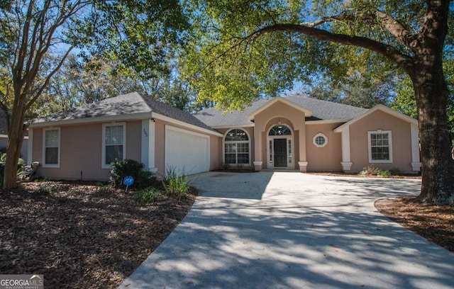 ranch-style house featuring a shingled roof, an attached garage, driveway, and stucco siding