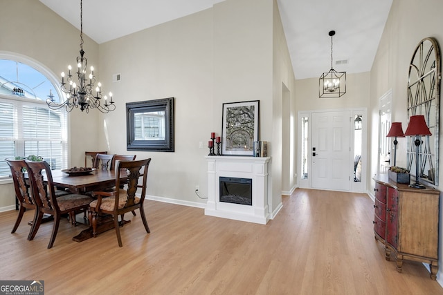 dining room with high vaulted ceiling, a notable chandelier, and light wood-type flooring