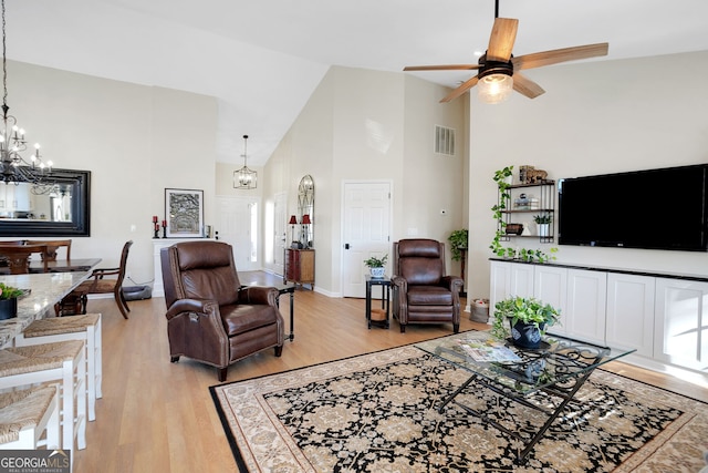 living room with ceiling fan with notable chandelier, light wood-type flooring, and high vaulted ceiling