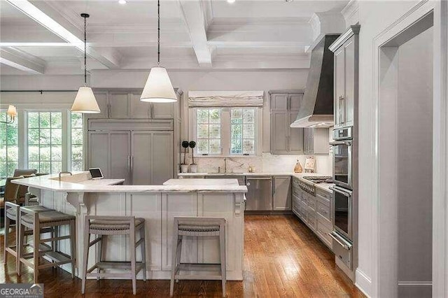 kitchen featuring beam ceiling, gray cabinets, decorative light fixtures, and wall chimney range hood