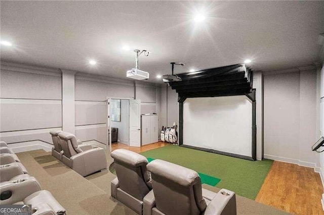 home theater room featuring wood-type flooring, golf simulator, and ornamental molding