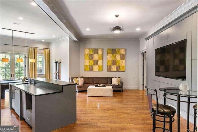 kitchen with french doors, crown molding, sink, hanging light fixtures, and an island with sink