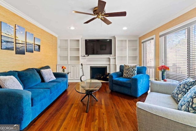 living room featuring a brick fireplace, built in shelves, ceiling fan, dark hardwood / wood-style floors, and ornamental molding