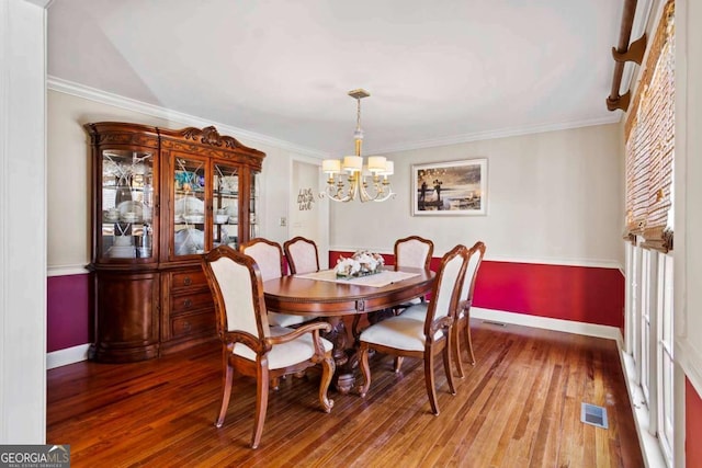 dining room with hardwood / wood-style flooring, ornamental molding, and an inviting chandelier