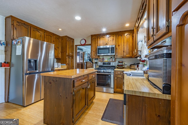 kitchen featuring sink, a center island, wood counters, appliances with stainless steel finishes, and light wood-type flooring