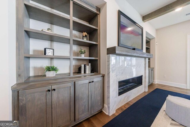 living room with built in shelves, ceiling fan, a fireplace, and beam ceiling