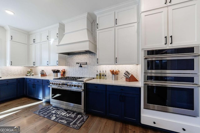 kitchen with blue cabinetry, premium range hood, white cabinetry, stainless steel appliances, and dark hardwood / wood-style floors