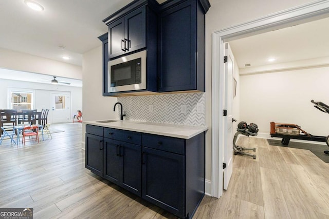 kitchen with stainless steel microwave, sink, ceiling fan, light hardwood / wood-style floors, and blue cabinetry