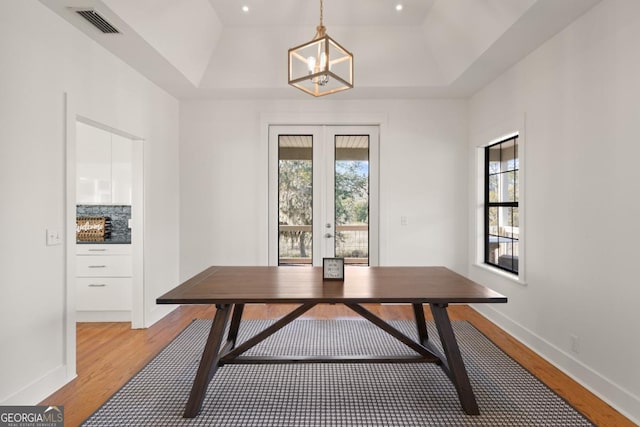 dining area featuring french doors, light hardwood / wood-style flooring, a raised ceiling, and a notable chandelier