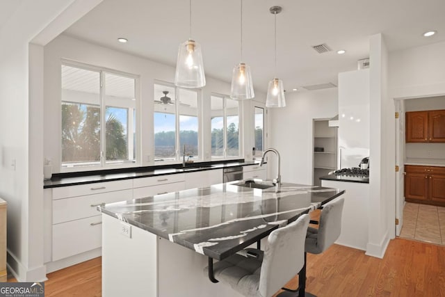 kitchen with sink, dark stone countertops, pendant lighting, light hardwood / wood-style floors, and white cabinets