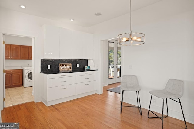 kitchen featuring white cabinets, a kitchen bar, washer / clothes dryer, and light hardwood / wood-style floors