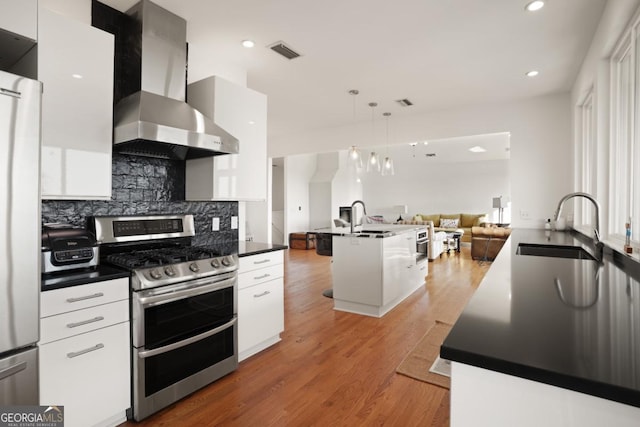 kitchen with white cabinets, pendant lighting, wall chimney range hood, and appliances with stainless steel finishes