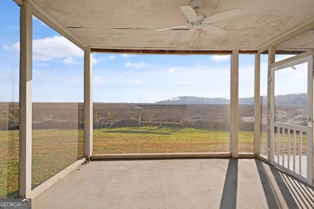 unfurnished sunroom featuring ceiling fan, a healthy amount of sunlight, and a rural view