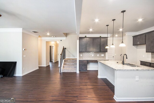 kitchen with a kitchen island with sink, light stone countertops, sink, dark brown cabinets, and tasteful backsplash