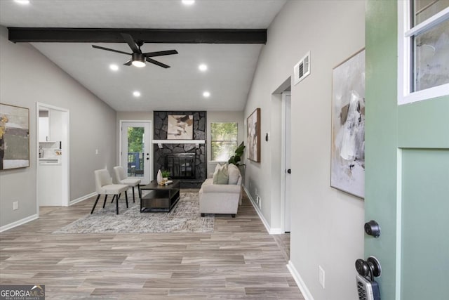 living room with vaulted ceiling with beams, ceiling fan, a stone fireplace, and light wood-type flooring