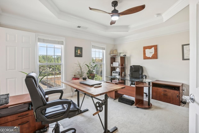 home office with ceiling fan, a raised ceiling, light colored carpet, and ornamental molding