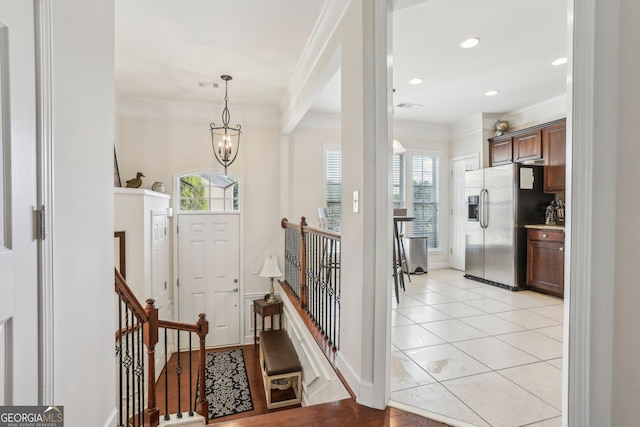 tiled foyer entrance with crown molding, a healthy amount of sunlight, and a notable chandelier