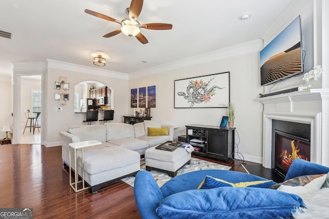 living room with crown molding, ceiling fan, and dark wood-type flooring