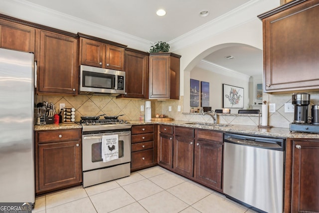 kitchen with stainless steel appliances, light stone counters, ornamental molding, and sink