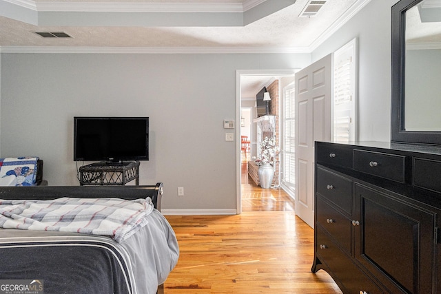 bedroom with a textured ceiling, a tray ceiling, light hardwood / wood-style flooring, and ornamental molding