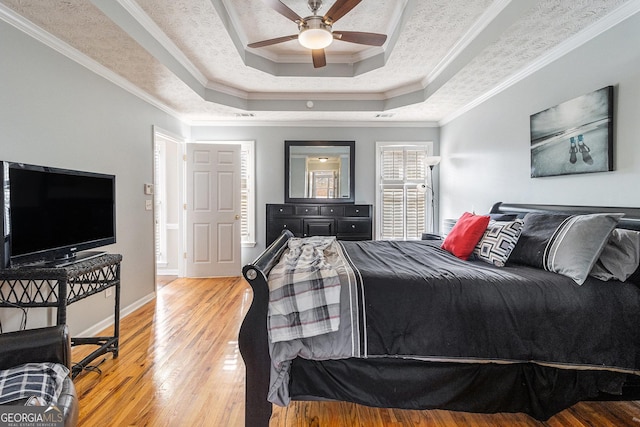 bedroom featuring a raised ceiling, crown molding, ceiling fan, a textured ceiling, and wood-type flooring