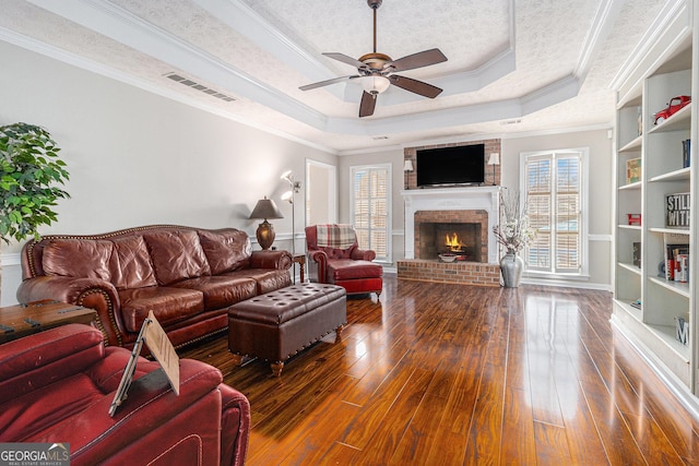 living room featuring ceiling fan, a raised ceiling, dark hardwood / wood-style floors, crown molding, and a fireplace