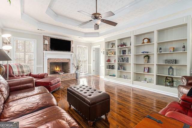 living room featuring a brick fireplace, ornamental molding, a textured ceiling, a raised ceiling, and dark wood-type flooring