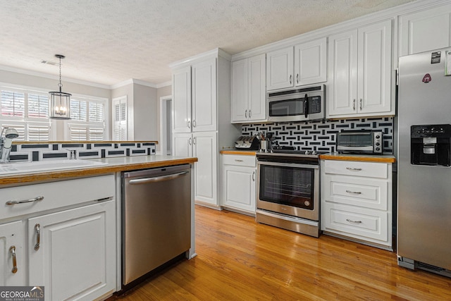 kitchen featuring ornamental molding, stainless steel appliances, white cabinets, light hardwood / wood-style floors, and hanging light fixtures