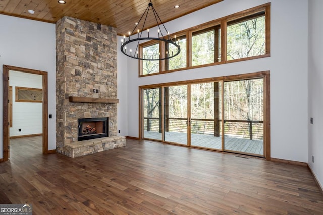 unfurnished living room featuring hardwood / wood-style flooring, a stone fireplace, a chandelier, and wooden ceiling