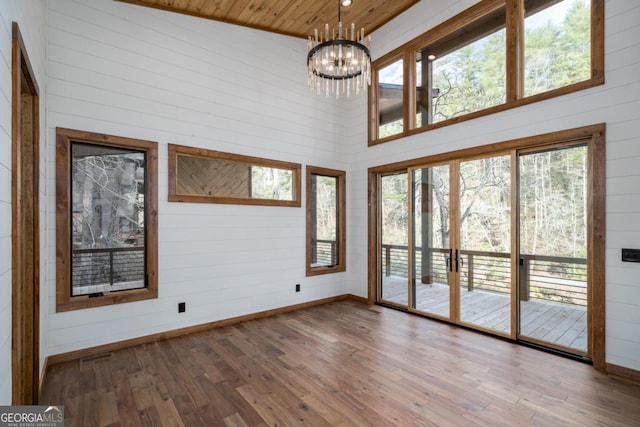 interior space with an inviting chandelier, wooden walls, a high ceiling, wood-type flooring, and wooden ceiling