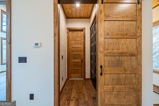 corridor featuring a barn door, dark hardwood / wood-style floors, wooden ceiling, and wood walls