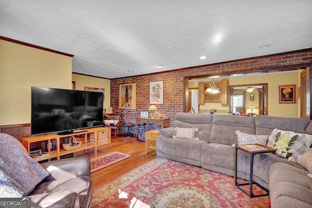 living room with light hardwood / wood-style floors, crown molding, a textured ceiling, and brick wall