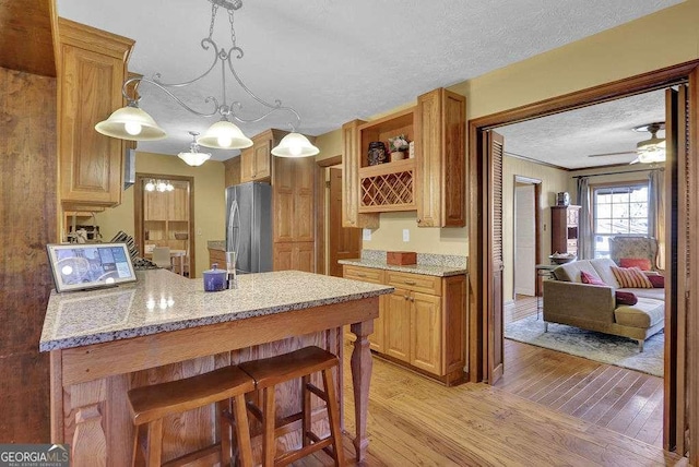 kitchen with a kitchen breakfast bar, stainless steel fridge, light wood-type flooring, a textured ceiling, and decorative light fixtures