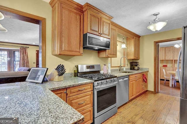 kitchen featuring sink, light hardwood / wood-style flooring, a textured ceiling, light stone counters, and stainless steel appliances